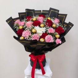 Bouquet of pink and red roses with white filler flowers and gold chocolates