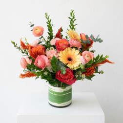 Mixed bouquet of pink, orange, and yellow flowers in a green-striped vase