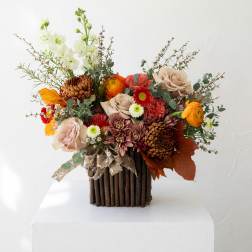 Mixed bouquet of roses, chrysanthemums, and orange blooms in a rustic wooden vase