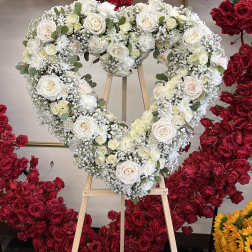 Heart-shaped white rose wreath on a wooden easel, surrounded by red roses