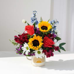 Bouquet of sunflowers, red roses, and daisies in a mug vase