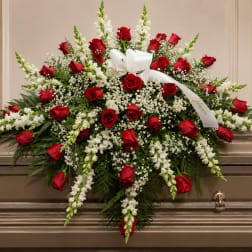 Red roses and white flowers arranged on a casket with a white ribbon