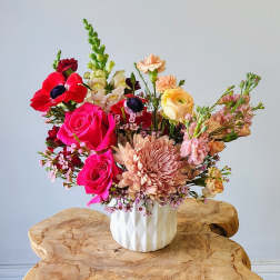 Mixed bouquet of pink, peach, and red flowers in a white vase