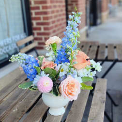 Pastel flower arrangement in a white vase with roses and blue delphinium