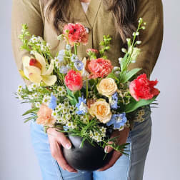 Mixed bouquet in a black vase with cream, pink, and blue flowers