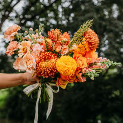 Handheld bouquet of orange and peach flowers tied with a ribbon
