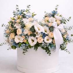 Low arrangement of white and peach flowers with blue accents in a round white hat box with ribbon