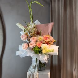 Pastel bouquet with pink roses, peach daisies, and tall white blooms in a glass vase