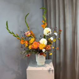 Tall floral arrangement in a white vase with orange, yellow, and white blooms