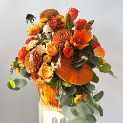 Orange floral arrangement with a pumpkin and small skeleton decoration
