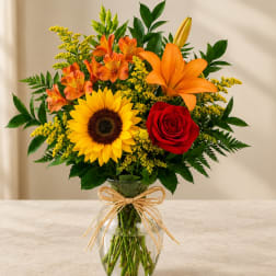 Bouquet of sunflowers, roses, lilies, and orange alstroemeria in a glass vase