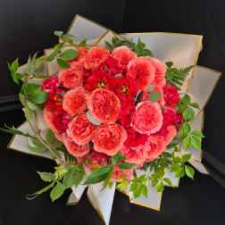 Bouquet of coral and red roses wrapped in white paper with gold trim