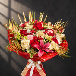 Bouquet of red and cream roses with a pink lily and gold palm fronds