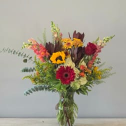 Mixed bouquet of sunflowers, gerbera daisies, roses, and snapdragons in a glass vase