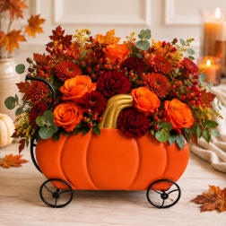 Pumpkin-shaped floral arrangement with orange and red blooms in a black metal cart.