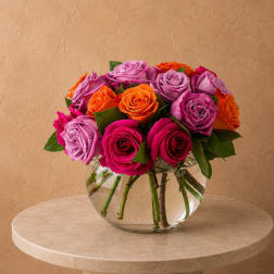 Mixed roses in pink, purple, and orange arranged in a clear glass bowl vase