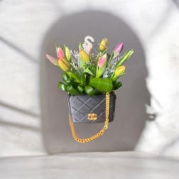 Tulips arranged in a black quilted handbag with a gold chain