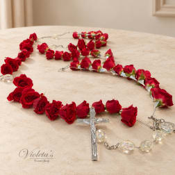 Red rose rosary with clear crucifix and bead accents on a table.
