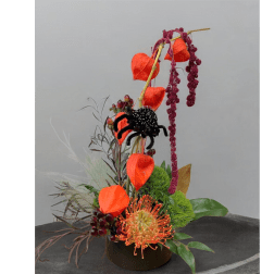 Tall floral arrangement with orange lantern-like blooms and a black spider accent in a dark vase.
