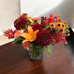 Mixed bouquet of red, orange, and pink flowers in a clear glass vase