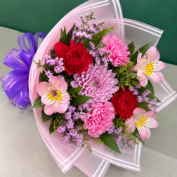 Bouquet of pink, red, and lavender flowers wrapped in pink paper with a purple ribbon
