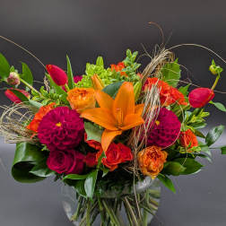 Bright mixed bouquet with orange lilies, red tulips, and magenta dahlias in a glass vase
