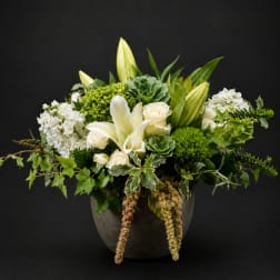 White lilies and roses arranged in a dark vase with green succulents