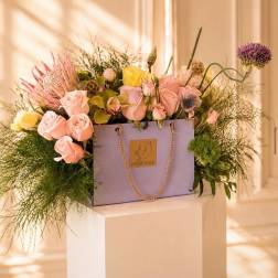 Lavender gift bag filled with pink and yellow roses and mixed blooms