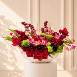 Large red and pink floral arrangement in a white bowl vase