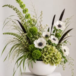Green and white floral arrangement in a white bowl vase