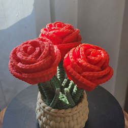 Three red rose-shaped flowers in a woven basket container