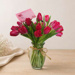 Pink tulips in a clear glass vase with a gold ribbon and card