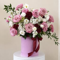Pink and white rose arrangement in a lavender hat box with a burgundy ribbon