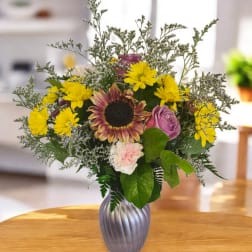 Mixed bouquet in a silver vase with a sunflower, yellow daisies, and pink roses