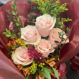 Bouquet of pale pink roses with mixed filler flowers wrapped in burgundy paper