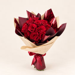 Bouquet of red roses wrapped in burgundy and cream paper with a ribbon