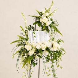 White floral standing arrangement on an easel with an open book centerpiece