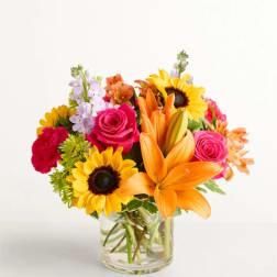 Bouquet of sunflowers, orange lilies, and pink roses in a glass vase