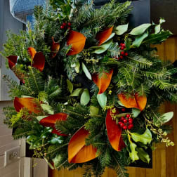 Holiday wreath with evergreen branches, red berries, and orange leaves