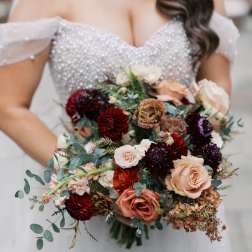 Bride holding a bouquet of blush, burgundy, and peach flowers