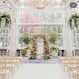 Floral wedding arch in a bright glass conservatory with rows of chairs