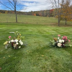 Two low floral arrangements on grass in an open field