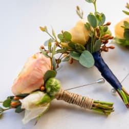 Small floral boutonnieres with peach and white blooms and greenery