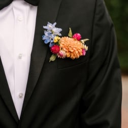 Boutonniere with peach and blue flowers on a black suit jacket