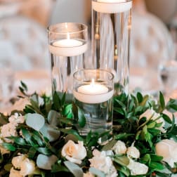 White roses and greenery surround three glass candle cylinders