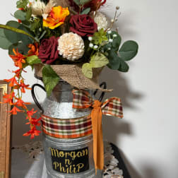 Mixed flowers in a metal milk can with plaid ribbon and a name plaque