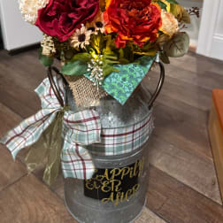 Floral arrangement in a metal milk can with plaid ribbon and a decorative sign