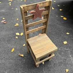Wooden chair with a star cutout on the backrest, sitting on pavement with scattered leaves.