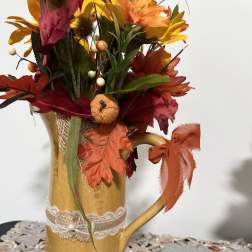 Autumn floral arrangement in a gold pitcher vase with ribbon and faux leaves