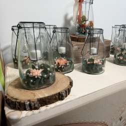 Glass lanterns with candles and small peach floral accents on wood slices